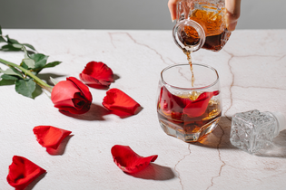 rose and rose petals on table while alcohol is being poured into a glass cup