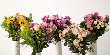 five mother's day bouquets in white vases