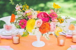 Bright pink, orange, and yellow flower centerpiece on table with a orange table cloth