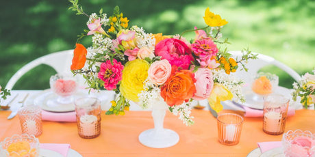 Bright pink, orange, and yellow flower centerpiece on table with a orange table cloth