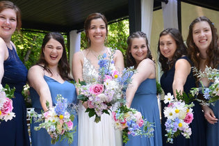 Bride with her five bridesmaids holding their purple, pink, and blue bouquets