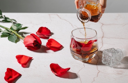 rose and rose petals on table while alcohol is being poured into a glass cup