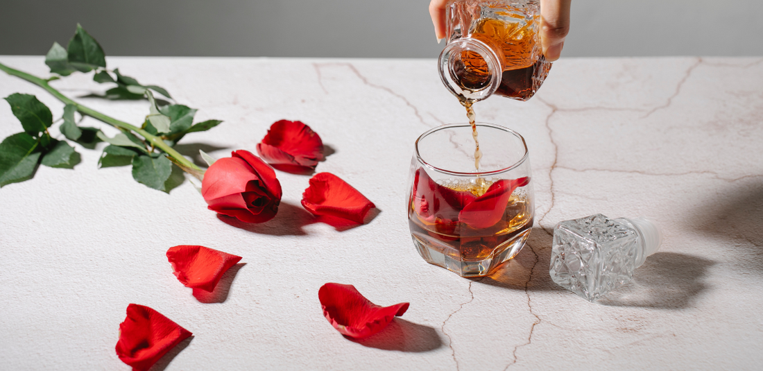 rose and rose petals on table while alcohol is being poured into a glass cup