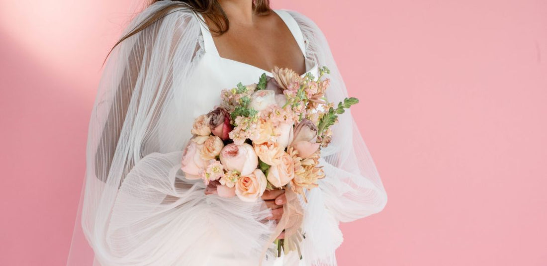bride holding perfectly peach bridal bouquet in front of pink background