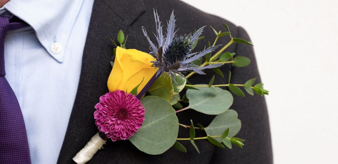 magenta pom, yellow spray rose, and blue thistle on a boutonniere