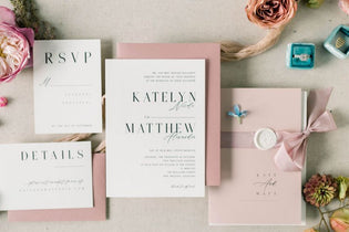 pink and white wedding invitation with a pink bow and pink flowers flat lay