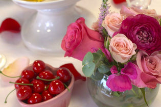 pink, red, and hot pink flower centerpiece next to a heart bowl full of cherries