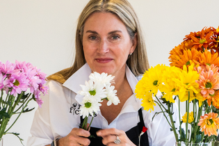 Liza Roeser holding white daisies and surrounded by pink, yellow, orange, and red daisies