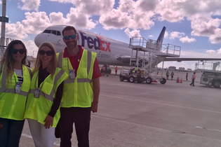 three people is neon yellow vests in front of a plane that says FedEx