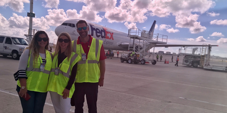 three people is neon yellow vests in front of a plane that says FedEx