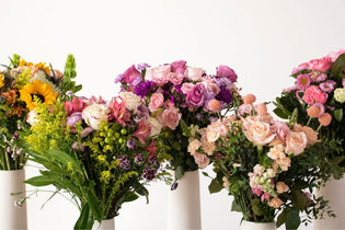 five mother's day bouquets in white vases