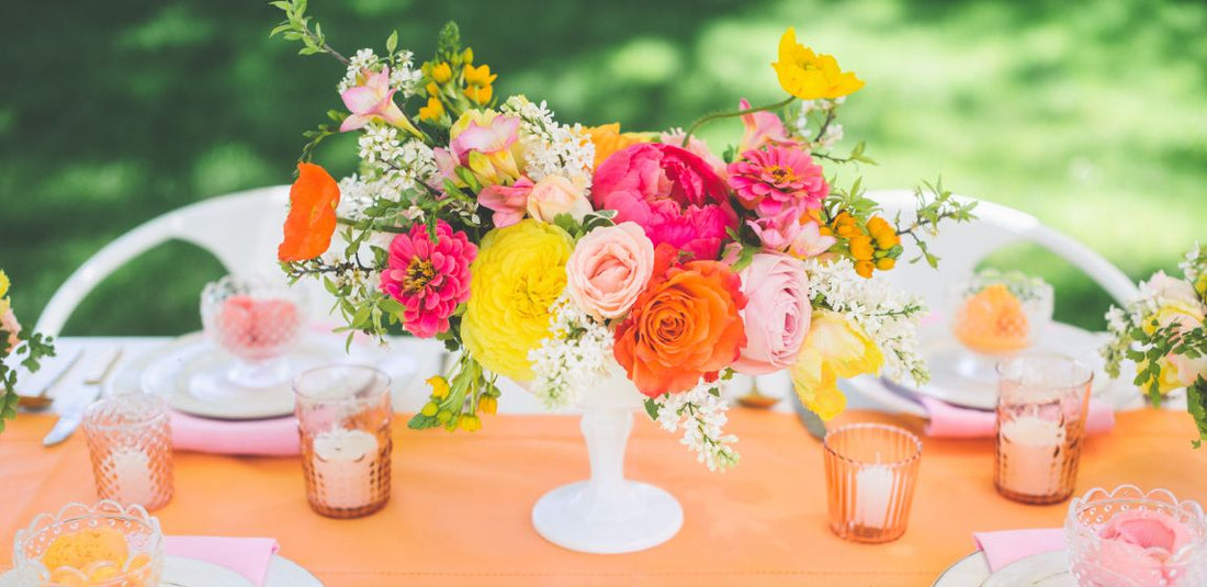 Bright pink, orange, and yellow flower centerpiece on table with a orange table cloth