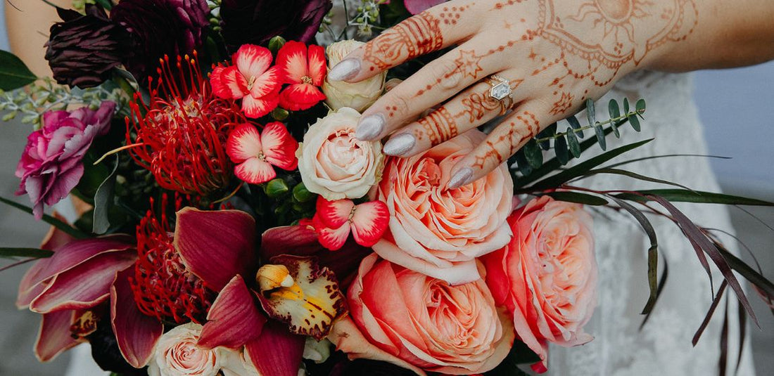 pink and red flower bouquet with hand that has henna on it is placed slightly over the flowers