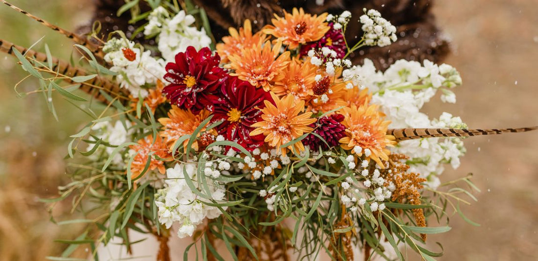 Bridal bouquet with orange, red, and white flowers in it being held by the bride