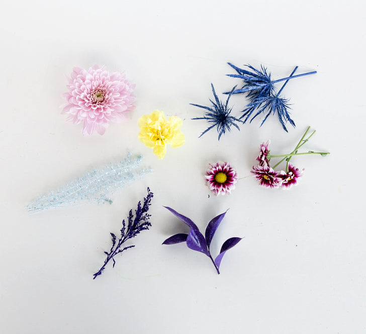 Flat lay of pink mum, yellow bloom, purple daisies and blue-dyed thistle and greenery