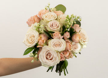 Hand holding a blush and ivory rose and spray rose bouquet with greenery